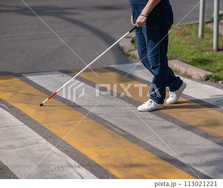 Close-up of the legs of a blind woman crossing the road at a crosswalk with a cane. Close-up of the legs of a blind woman crossing the road at a crosswalk with a cane. 113021221