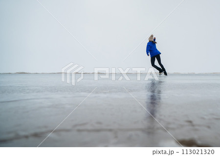 Caucasian woman in a blue sweater is skating on a frozen lake. The figure skater performs the program. Caucasian woman in a blue sweater is skating on a frozen lake. The figure skater performs the program. 113021320