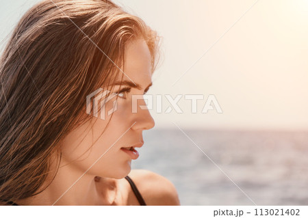 Woman summer travel sea. Happy tourist in hat enjoy taking picture outdoors for memories. Woman traveler posing on the beach at sea surrounded by volcanic mountains, sharing travel adventure journey 113021402