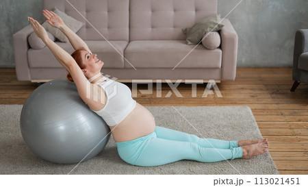 Pregnant red-haired woman doing exercises on fitness ball at home. Pregnant red-haired woman doing exercises on fitness ball at home. 113021451