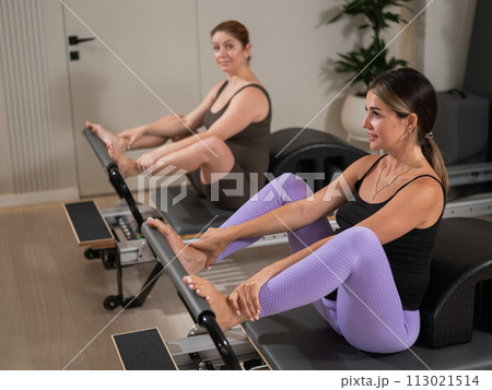 Two pregnant women do Pilates exercises on a reformer. Yoga class for pregnant women. Two pregnant women do Pilates exercises on a reformer. Yoga class for pregnant women. 113021514