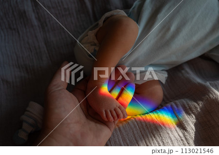 A man holds his newborn son by the leg. Beam of light through a prism.  113021546