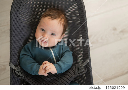 Cute newborn baby dressed in blue overalls sitting in a baby lounger. Cute newborn baby dressed in blue overalls sitting in a baby lounger. 113021909