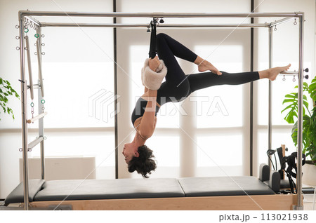 Asian woman doing aerial exercise on reformer machine.  113021938