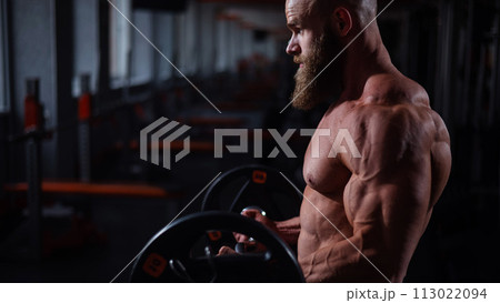 Caucasian bald topless man doing an exercise with a barbell in the gym. Bicep curls with weights. Caucasian bald topless man doing an exercise with a barbell in the gym. Bicep curls with weights. 113022094