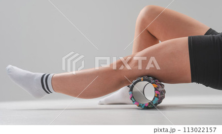 Faceless woman doing roller exercise for myofascial release on white background. Self-massage of legs.  113022157