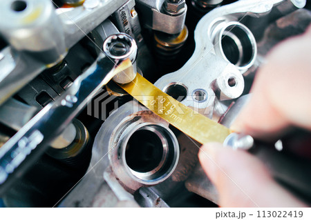 Car mechanic checking and adjusting valves of car engine with feeler gauge or thickness gauge tool 113022419