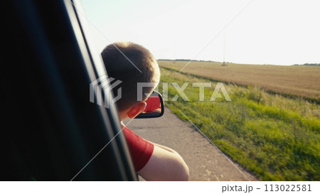 child boy son enjoys summer day with his hand out car window, car rushing along road, child feels wind freedom, car carries child family journey along picturesque road, child car, moving unison with 113022581