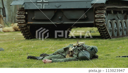 Close Up View On Re-enactor Dressed As German Wehrmacht Soldier Lies Slain In Reconstruction Of Battles World War Ii Near Wehrmacht Light Panzer Tank. German Infantry Soldier In World War Ii 113023947