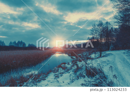 Rural landscape in winter. View of the brook and cloudy sky at sunset. 113024233