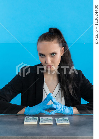 A young cashier in a bank behind a glass holds a bundle of banknotes on the counter. A young cashier in a bank behind a glass holds a bundle of banknotes on the counter. 113024400