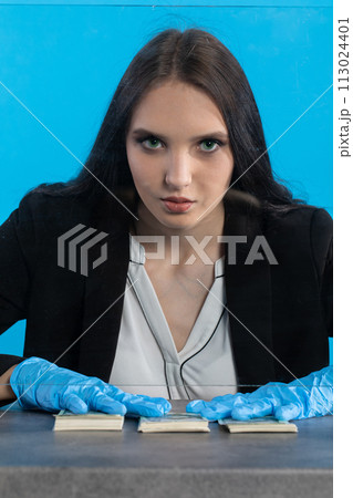 A young cashier in a bank behind a glass holds a bundle of banknotes on the counter. A young cashier in a bank behind a glass holds a bundle of banknotes on the counter. 113024401