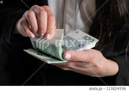 The woman is counting exactly one hundred zlotys paper banknotes. 113024536