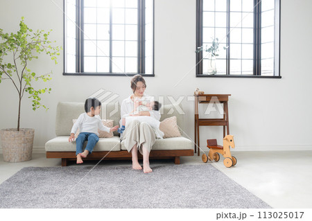 明るいリビングのソファで赤ちゃんにミルクをあげながら 明るいリビングのソファで赤ちゃんにミルクをあげながら 113025017