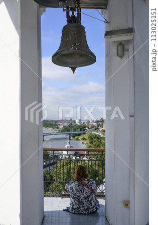 The bell on the belfry of the medieval Spaso-Preobrazhensky Monastery, and a woman admiring the view 113025151