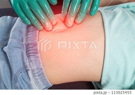 A surgeon doctor palpates the abdomen of the peri-umbilical zone during an abdominal hernia in a little girl. The concept of an extended umbilical ring, abdominal tension, umbilical hernia in A surgeon doctor palpates the abdomen of the peri-umbilical zone during an abdominal hernia in a little girl. The concept of an extended umbilical ring, abdominal tension, umbilical hernia in 113025455