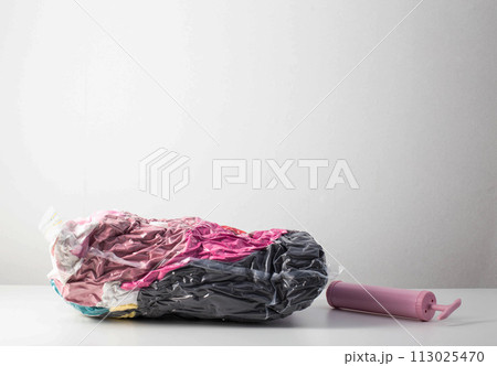 Pink hand pump for pumping air out of a bag with things on a white background. Modern technology for compact storage of things and clothes. Copy space for text 113025470