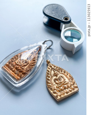 Thai old buddha amulet with magnifier on the background Thai old buddha amulet with magnifier on the background 113025913