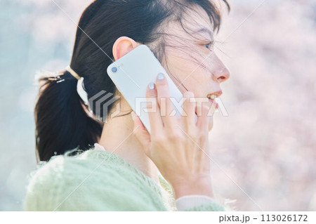 桜の下スマホで通話する女性 113026172