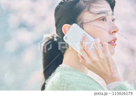 桜の下スマホで通話する女性 113026179