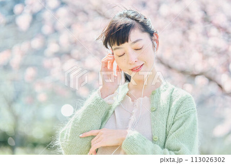 桜の中で音楽を聴く女性 113026302