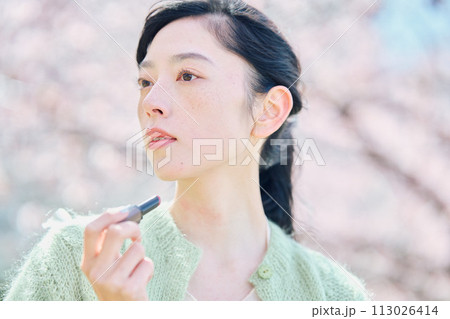 桜の中リップを塗る女性 113026414
