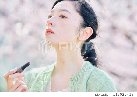 桜の中リップを塗る女性 113026415