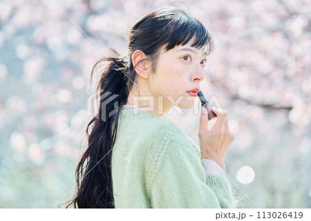 桜の中リップを塗る女性 113026419