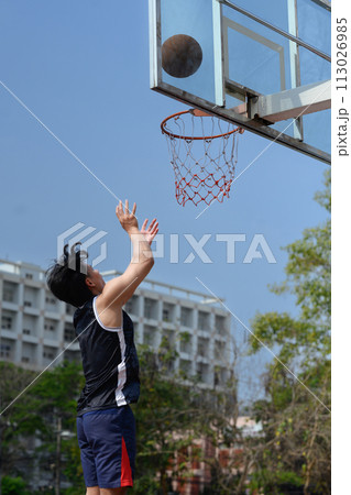Shot of basketball player throwing a ball toward basket, training on the urban basketball court 113026985