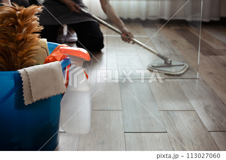 Basket with cleaning items on blurred background woman wiping floor in the living room 113027060