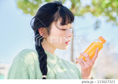新緑の公園でオレンジジュースを飲む女性 113027321