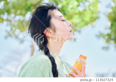 新緑の公園でオレンジジュースを飲む女性 新緑の公園でオレンジジュースを飲む女性 113027324