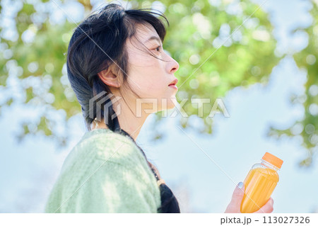 新緑の公園でオレンジジュースを飲む女性 113027326