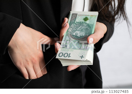 The woman holds her right hand in her pocket and squeezes a thick bundle of banknotes in her left. 113027485