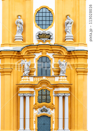 The ornate yellow and white baroque facade of Melk Abbey, adorned with sculptures and decorative windows, reflecting the grandeur of the historic monastery. Austria 113028016