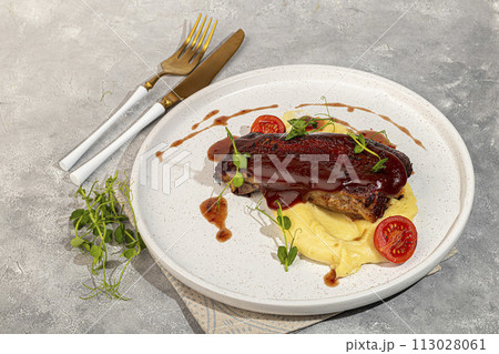 Beef on the bone with mashed potatoes, topped with red sauce and cherry tomatoes. 113028061
