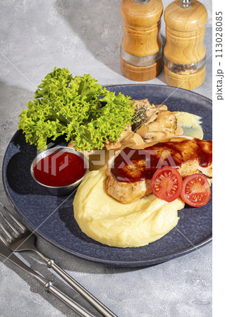 Mashed potatoes with chicken breast in red sauce with lettuce and tomato slices. 113028085