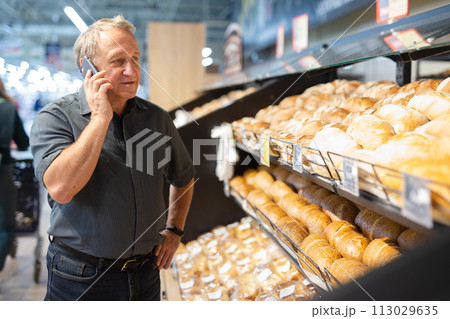 Man takes muffins on shelf of bakery section 113029635
