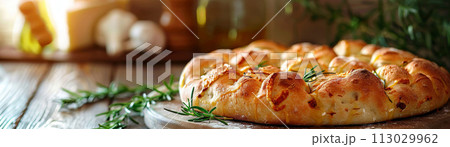Homemade focaccia bread garnished with fresh rosemary and sesame seeds, served on a rustic wooden board next to olive oil 113029962