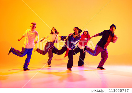 Modern dance crew in synch motion performing hip-hop in neon light against gradient colorful studio background. Modern dance crew in synch motion performing hip-hop in neon light against gradient colorful studio background. 113030757
