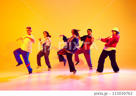 Dynamic portrait of young talented dancers dressed streetstyle clothes dancing in motion in neon light against gradient studio background. 113030762