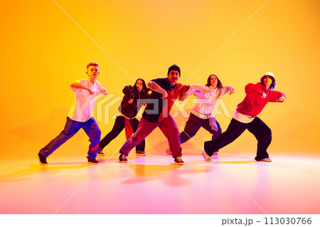 Energetic dance team performing contemporary dance moves in neon light against gradient colorful studio background. 113030766
