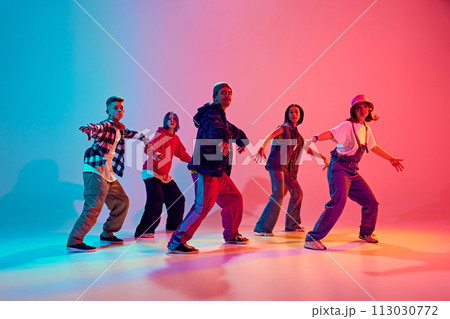 Energetic young dancers in street fashion clothes dance in neon light against gradient colorful studio background. Energetic young dancers in street fashion clothes dance in neon light against gradient colorful studio background. 113030772