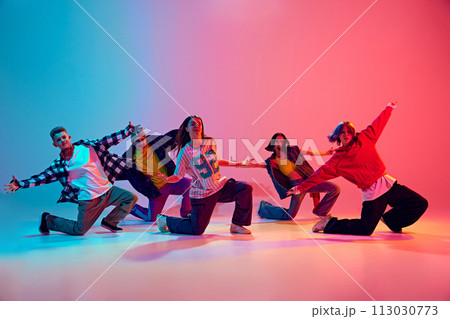 Dynamic squad of young dancers performing their routine in neon light against gradient colorful studio background. 113030773