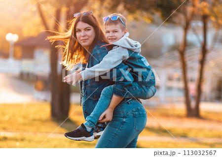 A smiling young mother and son play in an autumn park. The concept of a happy childhood A smiling young mother and son play in an autumn park. The concept of a happy childhood 113032567