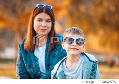 Portrait of young smiling mother and her son. In the background is autumn park. The concept of a happy childhood Portrait of young smiling mother and her son. In the background is autumn park. The concept of a happy childhood 113032573