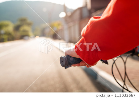 Sports lifestyle. A woman rides a Bicycle. Hand with the steering wheel close-up. Empty road in the background. Copy space Sports lifestyle. A woman rides a Bicycle. Hand with the steering wheel close-up. Empty road in the background. Copy space 113032667
