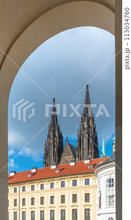 The twin spires of St. Vitus Cathedral rise majestically above Prague Castle, framed by an archway under a cloudy sky. Prague, Czechia The twin spires of St. Vitus Cathedral rise majestically above Prague Castle, framed by an archway under a cloudy sky. Prague, Czechia 113034760