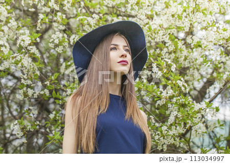 Cute fashion model with long brown hair and natural makeup against floral background outdoor 113034997