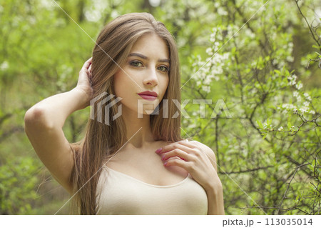 Posing young woman with natural makeup and healthy long brown hair in blossom park outdoors. Posing young woman with natural makeup and healthy long brown hair in blossom park outdoors. 113035014